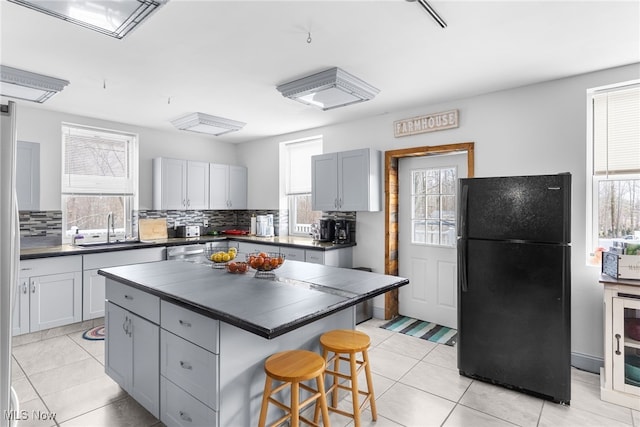 kitchen with a sink, a kitchen breakfast bar, backsplash, dark countertops, and freestanding refrigerator