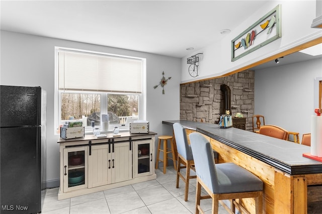 kitchen with a wood stove, light tile patterned floors, and freestanding refrigerator