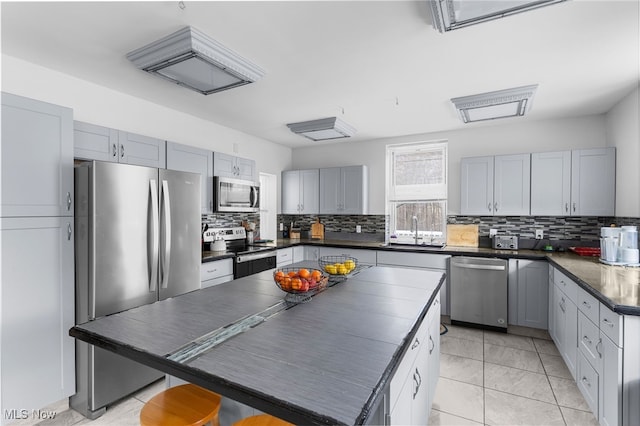 kitchen featuring dark countertops, backsplash, appliances with stainless steel finishes, and a sink