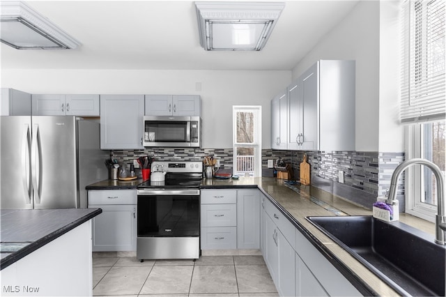 kitchen featuring dark countertops, decorative backsplash, appliances with stainless steel finishes, light tile patterned flooring, and a sink