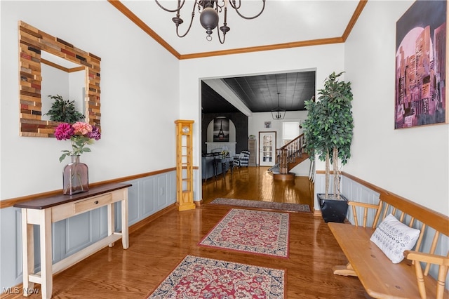 corridor featuring stairs, a notable chandelier, wainscoting, and crown molding