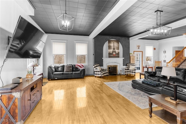 living room with light wood-style flooring, an inviting chandelier, a glass covered fireplace, and stairway