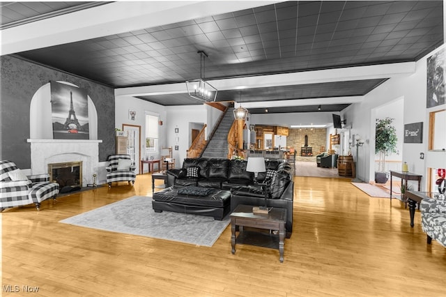 living area featuring beam ceiling, wood finished floors, a fireplace, and a chandelier