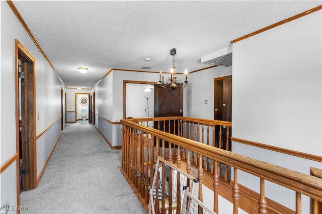 hall featuring light colored carpet, ornamental molding, an upstairs landing, an inviting chandelier, and a textured ceiling