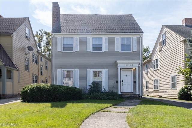 colonial-style house featuring roof with shingles, a chimney, and a front lawn