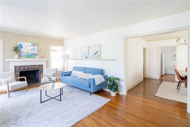 living room featuring a tiled fireplace, a textured ceiling, wood finished floors, and ornamental molding