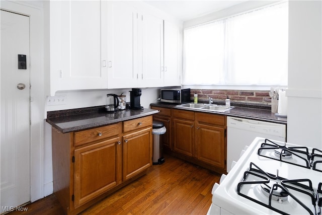 kitchen featuring white appliances, brown cabinetry, a sink, dark wood-type flooring, and dark countertops