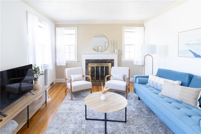 living area featuring a fireplace with flush hearth, ornamental molding, a textured ceiling, wood finished floors, and baseboards