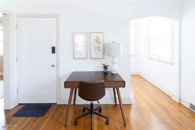 home office with light wood-style floors, baseboards, and arched walkways