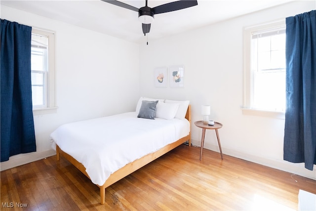 bedroom with ceiling fan, baseboards, multiple windows, and wood finished floors