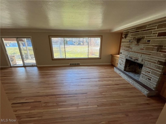 unfurnished living room featuring baseboards, visible vents, light wood-style flooring, a fireplace, and a textured ceiling