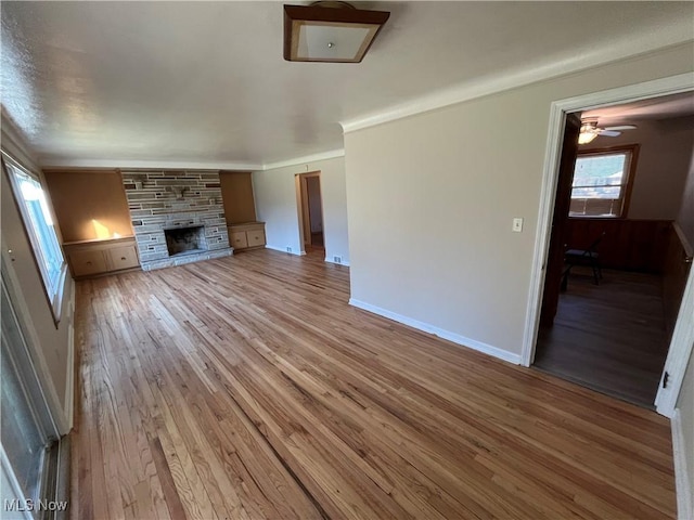 unfurnished living room featuring ceiling fan, a fireplace, baseboards, wood finished floors, and ornamental molding