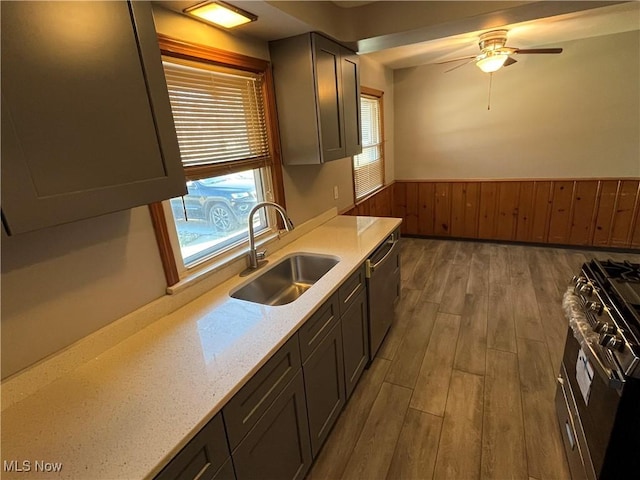 kitchen with a ceiling fan, wood finished floors, a sink, a wainscoted wall, and stainless steel appliances