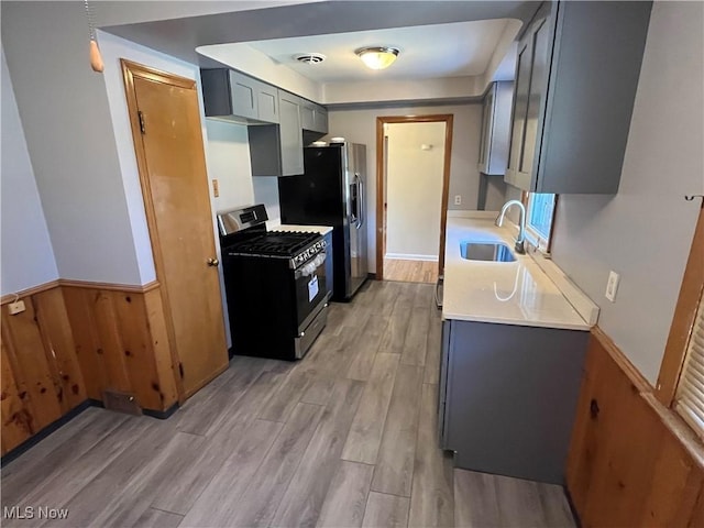 kitchen featuring light wood-type flooring, light countertops, a sink, appliances with stainless steel finishes, and gray cabinetry