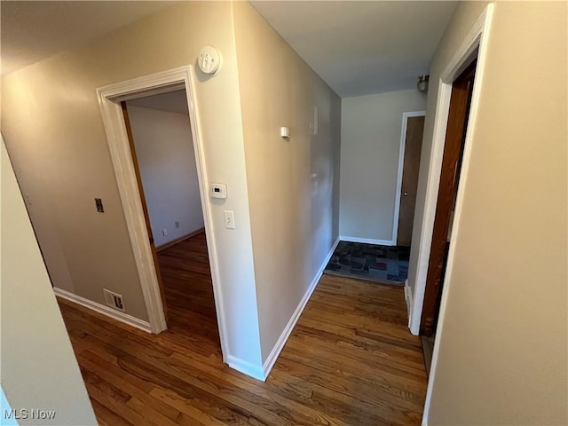 corridor with baseboards, wood finished floors, and visible vents