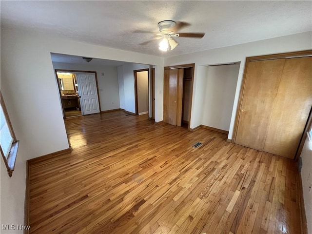 unfurnished bedroom with baseboards, ceiling fan, two closets, and light wood-style floors