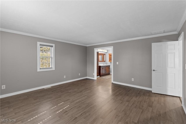 empty room with visible vents, wood finished floors, baseboards, and ornamental molding