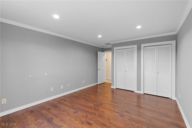 unfurnished bedroom featuring baseboards, crown molding, multiple closets, and wood finished floors