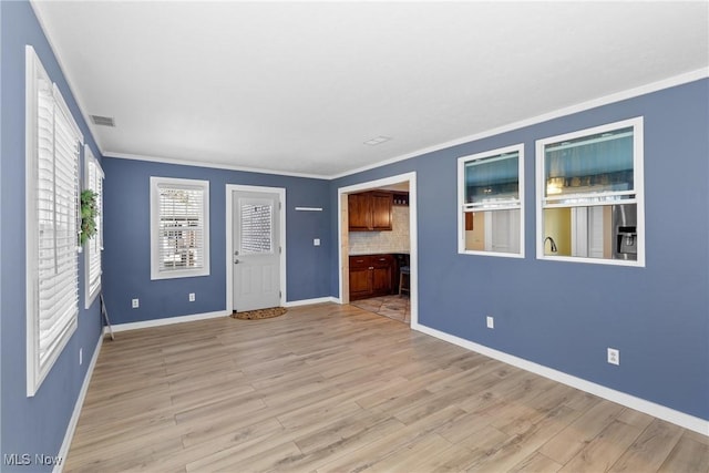 spare room featuring visible vents, baseboards, light wood-style flooring, and crown molding