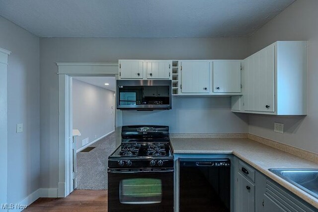 kitchen featuring light countertops, white cabinetry, a sink, dark wood finished floors, and black appliances