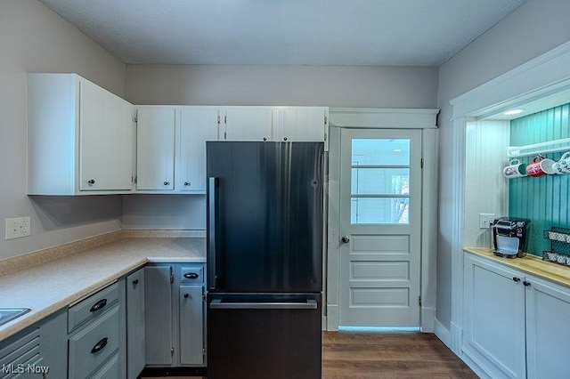 kitchen with dark wood-type flooring, light countertops, white cabinets, and black refrigerator