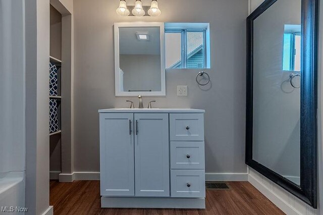 full bath with baseboards, plenty of natural light, vanity, and wood finished floors