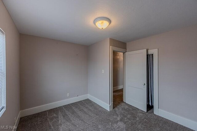 unfurnished bedroom featuring baseboards, multiple windows, and dark colored carpet
