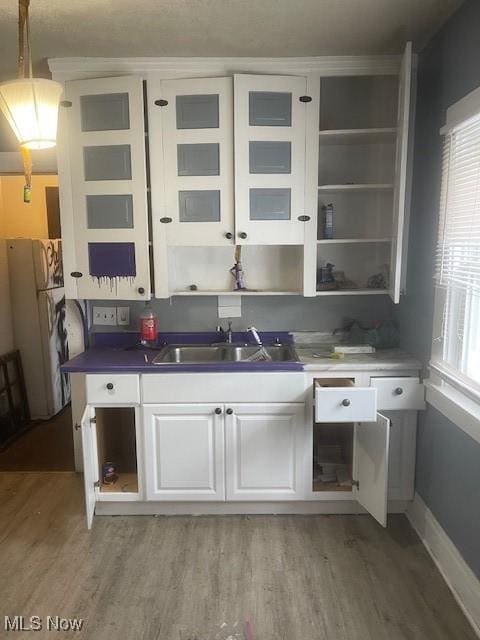 kitchen featuring light wood finished floors, open shelves, freestanding refrigerator, a sink, and white cabinets