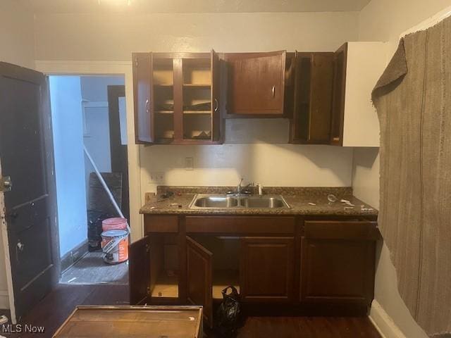 kitchen featuring dark countertops, a sink, glass insert cabinets, dark brown cabinetry, and dark wood-style flooring