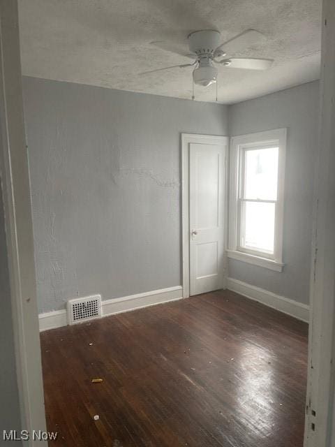 empty room with visible vents, ceiling fan, baseboards, and wood finished floors