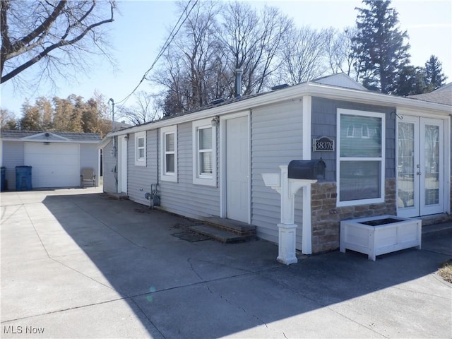 view of side of property featuring an outbuilding, concrete driveway, french doors, stone siding, and a detached garage