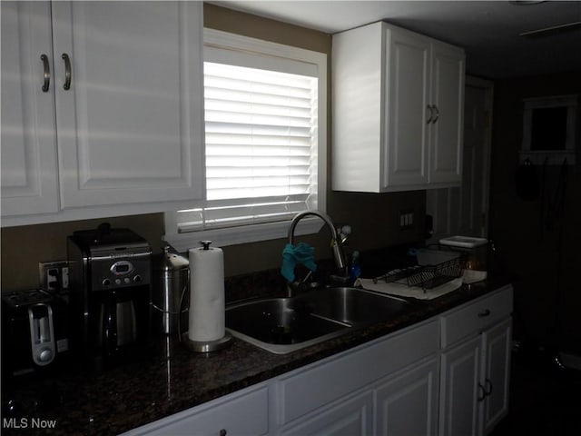 kitchen featuring a sink, dark stone counters, and white cabinets