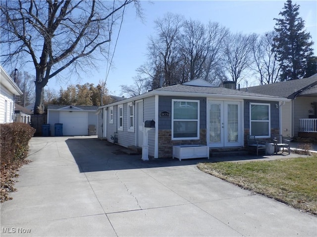 view of property exterior featuring french doors, stone siding, an outbuilding, and driveway