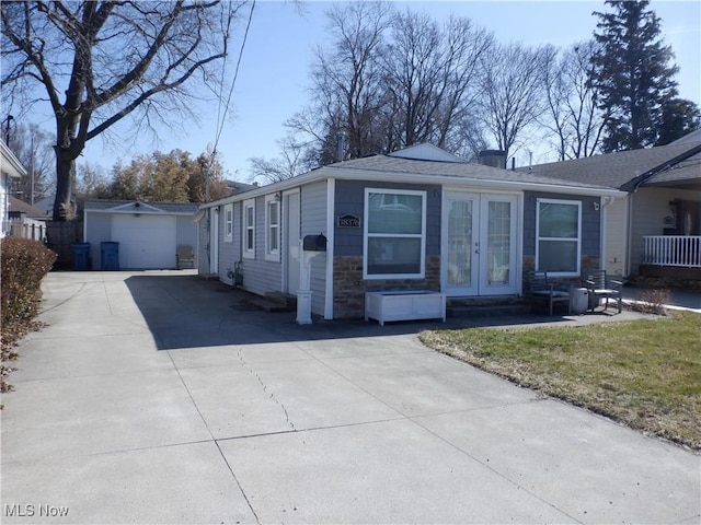 view of front facade with concrete driveway, french doors, a garage, an outbuilding, and stone siding