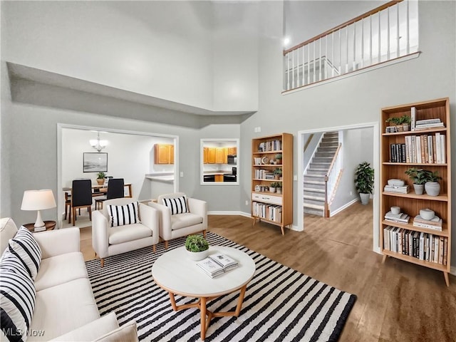 living room featuring stairway, wood finished floors, baseboards, a towering ceiling, and a notable chandelier