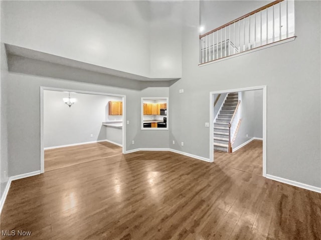 unfurnished living room featuring wood finished floors, baseboards, a high ceiling, stairs, and a notable chandelier