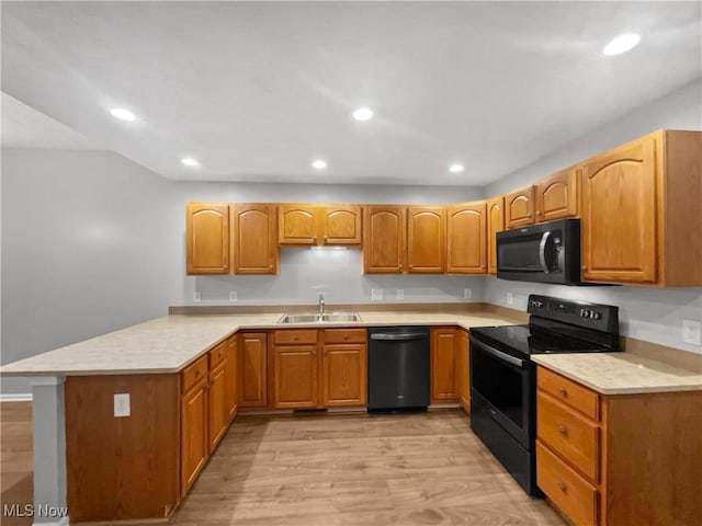 kitchen with light wood finished floors, light countertops, a peninsula, black appliances, and a sink