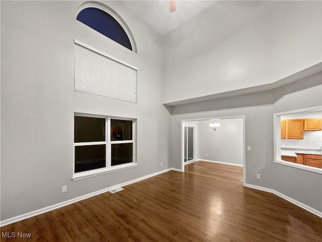 unfurnished living room with visible vents, baseboards, a high ceiling, and dark wood finished floors