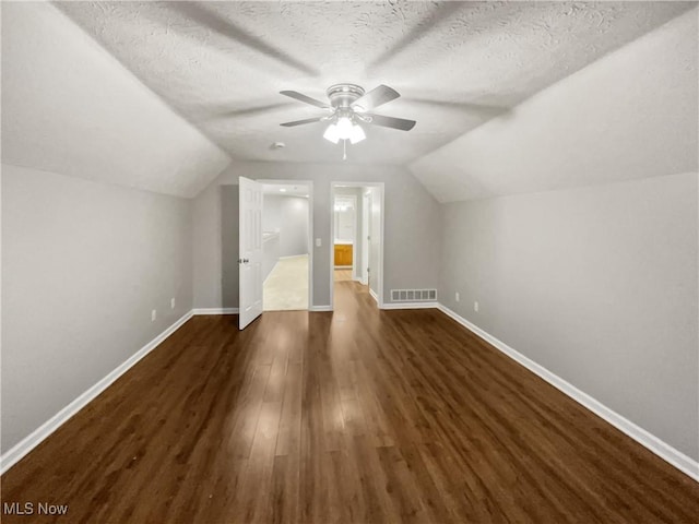 additional living space with dark wood-type flooring, baseboards, visible vents, and a textured ceiling