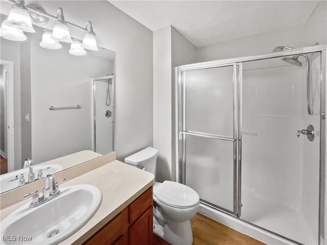 bathroom featuring wood finished floors, toilet, a stall shower, and vanity