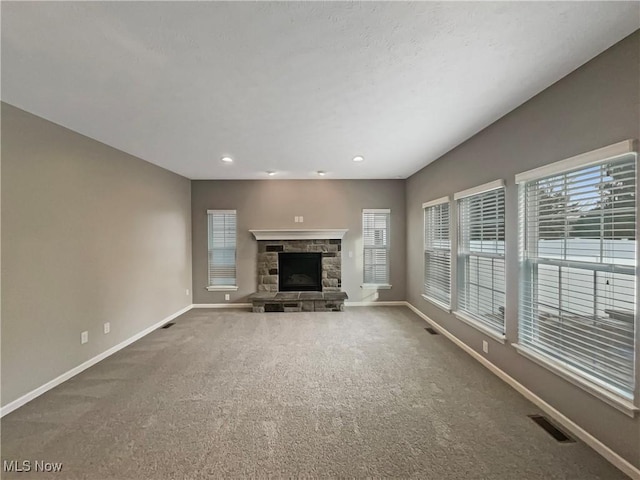 unfurnished living room with a stone fireplace, baseboards, visible vents, and carpet floors