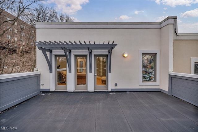 entrance to property with stucco siding, a pergola, and a patio