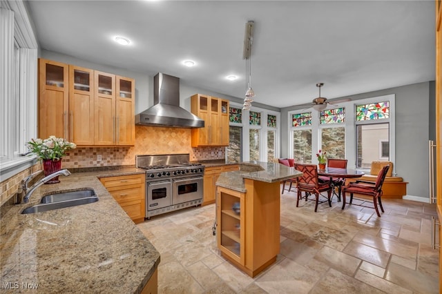 kitchen with a sink, double oven range, tasteful backsplash, stone tile flooring, and wall chimney exhaust hood