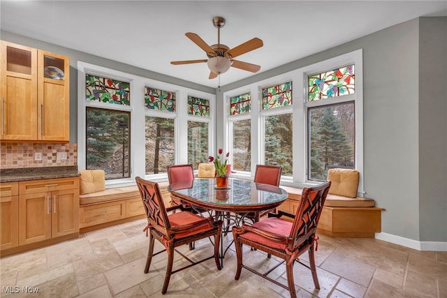 dining room featuring baseboards, stone tile floors, and a ceiling fan