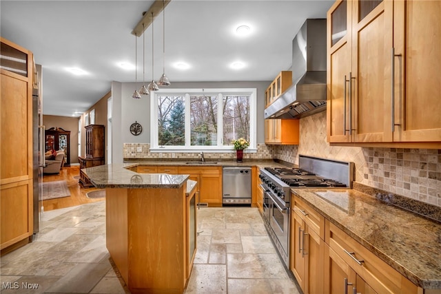 kitchen featuring wall chimney range hood, dark stone counters, stone tile flooring, stainless steel appliances, and a sink