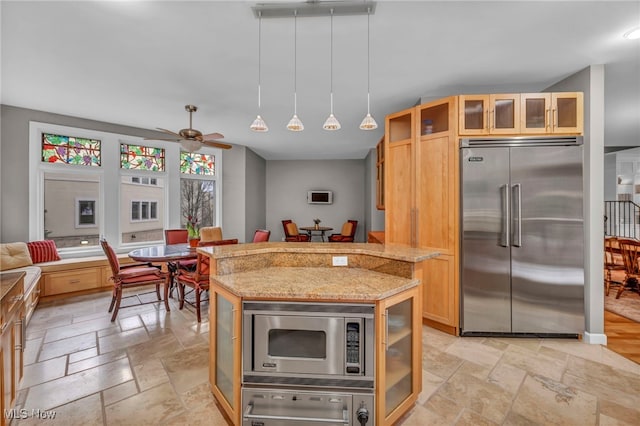 kitchen featuring light stone counters, ceiling fan, stone tile flooring, glass insert cabinets, and built in appliances