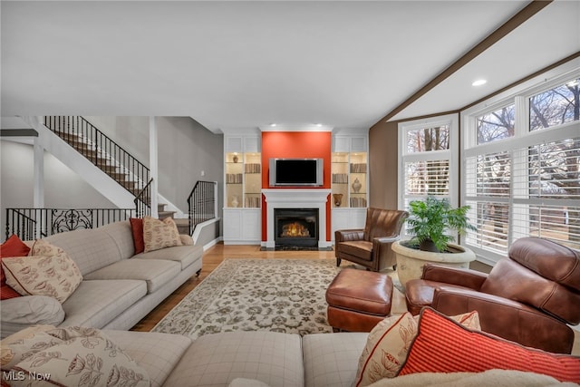 living room with stairway, plenty of natural light, wood finished floors, and a fireplace with flush hearth