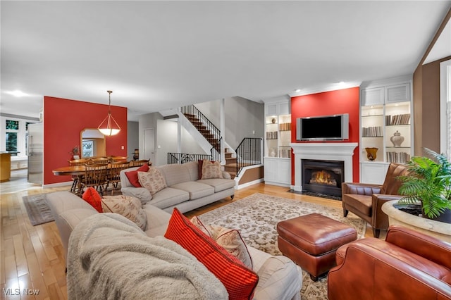 living room with stairway, light wood-style floors, and a fireplace with flush hearth