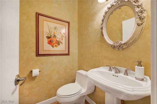 bathroom featuring toilet, baseboards, and a sink