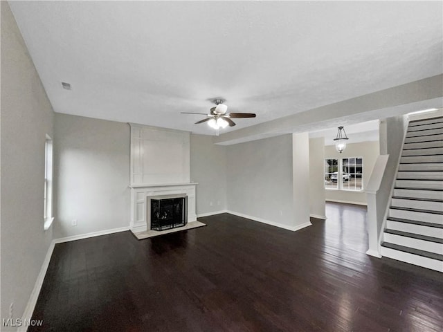 unfurnished living room featuring stairs, a large fireplace, baseboards, ceiling fan, and dark wood-style flooring